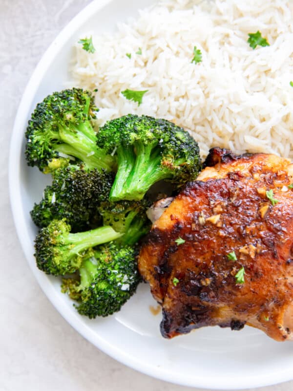 overhead view of air fryer broccoli on a white plate with chicken and rice.