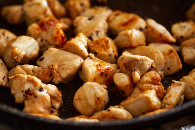 cubes of chicken cooking in a pan.