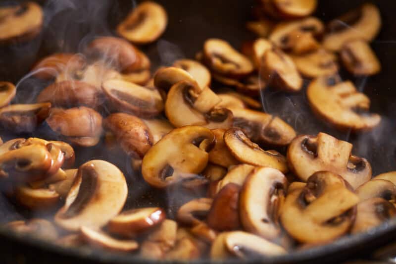 sliced mushrooms cooking in a pan.