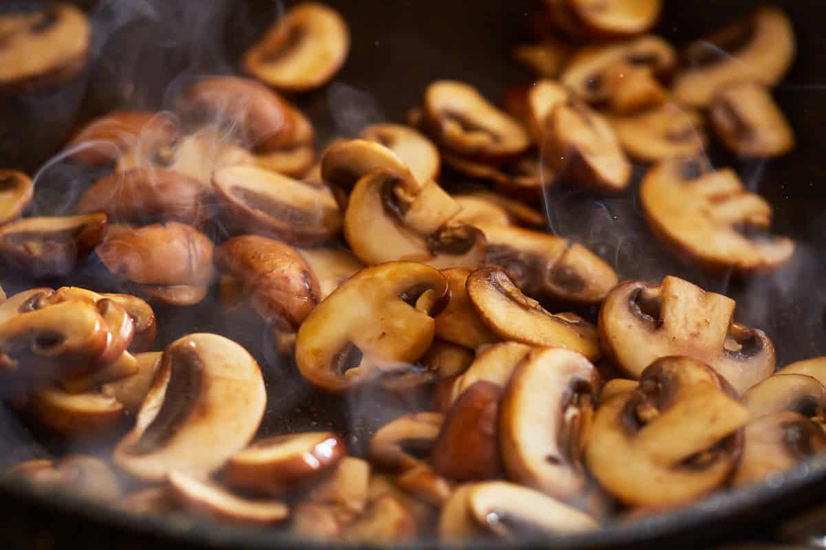 sliced mushrooms cooking in a pan.